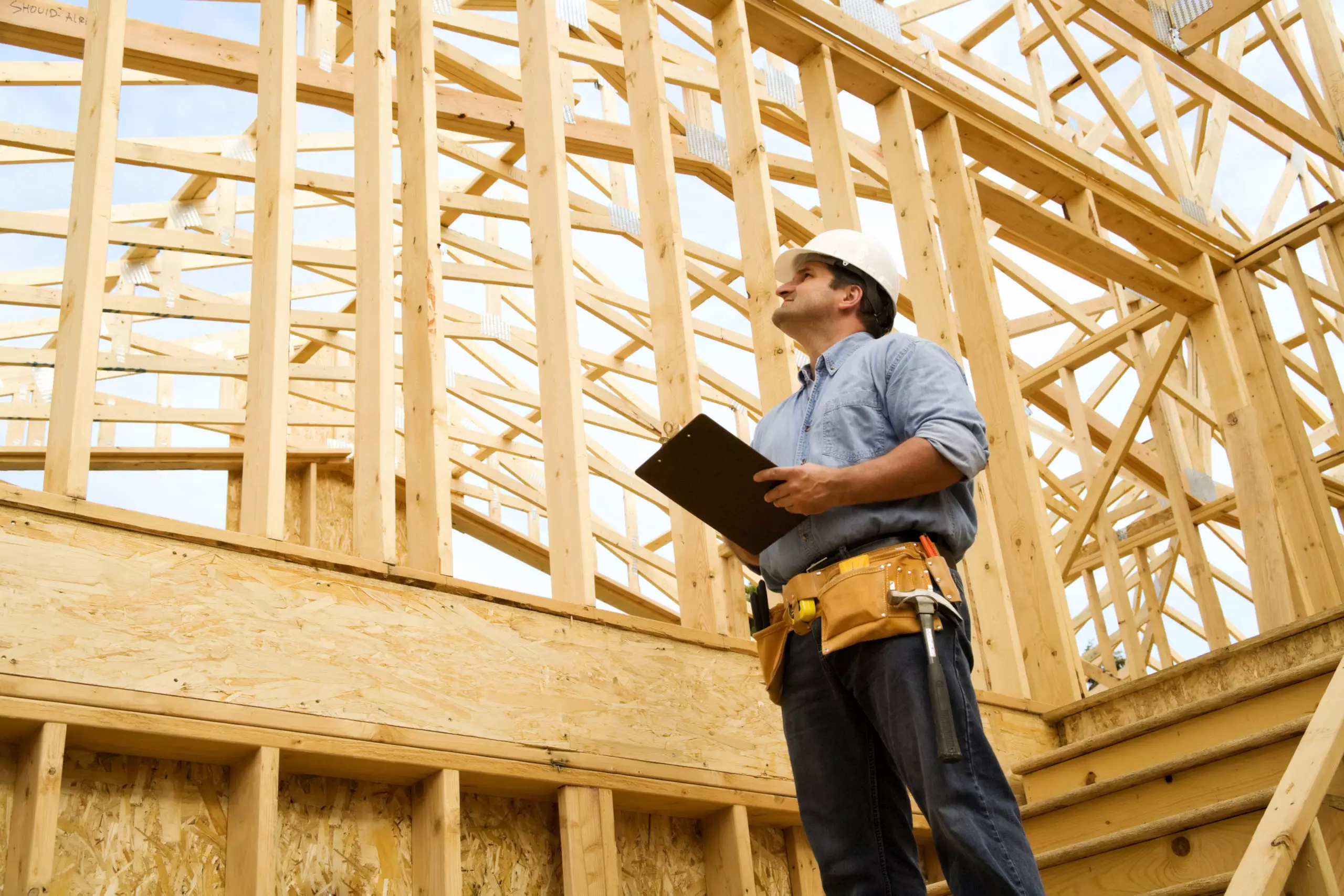 A man looking up at a wood frame of a building in mid-construction